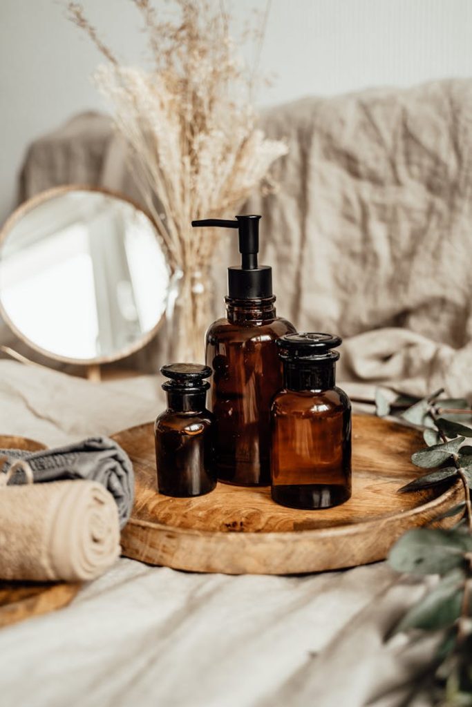 Stylish brown glass bottles for aromatherapy set on a wooden tray with towels and dried plants.